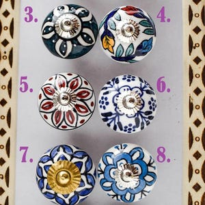 May include: A collection of ten decorative ceramic cabinet knobs. Each knob features a unique hand-painted floral design in various colors, including blue, red, and green, with a silver metal base. The knobs are arranged in a grid.