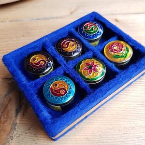 Peut inclure: Un ensemble de six petites boîtes rondes décoratives avec des motifs complexes, dont un symbole yin-yang et des motifs floraux. Les boîtes sont dans un plateau en velours bleu. Les couvercles des boîtes présentent diverses couleurs, dont l'or, le rouge, le vert et le bleu.
