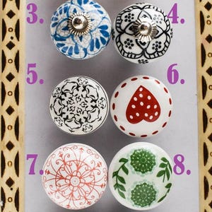 Puede incluir: Una colección de diez pomos de cerámica decorativos para armarios. Los pomos presentan varios patrones coloridos, incluyendo diseños florales, corazones y formas geométricas. Cada pomo tiene una base metálica para la fijación.
