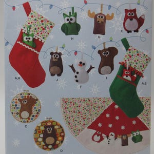 May include: Simplicity pattern 1516 featuring Christmas stocking and ornament designs. The pattern includes various felt ornaments like owls, moose, and bears, along with a tree skirt. The background is light blue with snowflake accents.