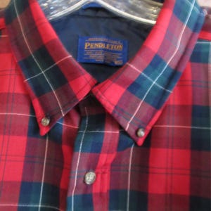 May include: A red, black, and green plaid button-down shirt with a blue collar lining. The shirt has a Pendleton label. The shirt is buttoned at the collar and down the front.