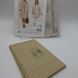 May include: A sewing pattern from Burda Style, featuring a coat and jacket design. The pattern packet includes images of the finished garments and the number 6802. A stack of folded pattern pieces is in the foreground.