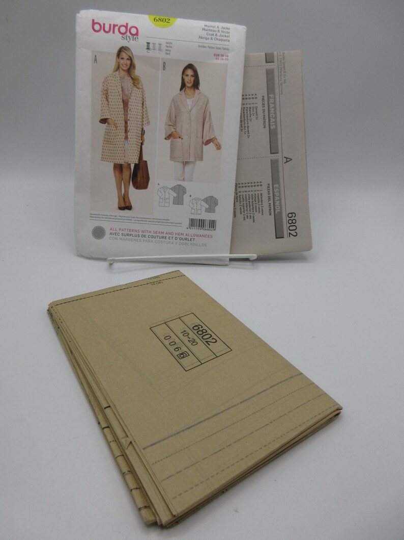 May include: A sewing pattern from Burda Style, featuring a coat and jacket design. The pattern packet includes images of the finished garments and the number 6802. A stack of folded pattern pieces is in the foreground.