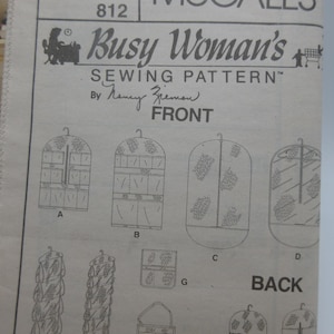 May include: A vintage McCall's sewing pattern titled "Busy Woman's Sewing Pattern" by Nancy Zieman. The pattern features various garment storage designs, including hanging organizers and garment bags, with detailed illustrations and diagrams.