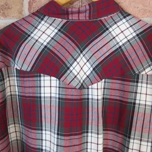 Puede incluir: Primer plano de una camisa a cuadros en tonos rojos, blancos, verdes y grises. La camisa presenta un patr&oacute;n de cuadros cl&aacute;sico con una pieza de estilo occidental en la espalda. La tela parece ser de algod&oacute;n o mezcla de peso medio.