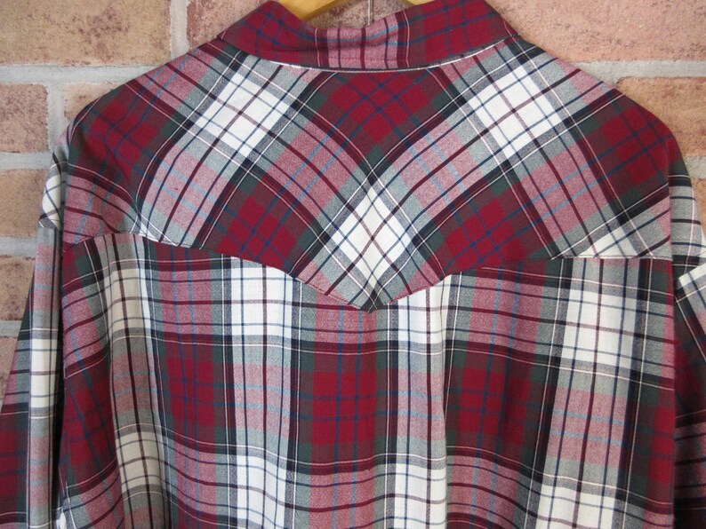 Puede incluir: Primer plano de una camisa a cuadros en tonos rojos, blancos, verdes y grises. La camisa presenta un patr&oacute;n de cuadros cl&aacute;sico con una pieza de estilo occidental en la espalda. La tela parece ser de algod&oacute;n o mezcla de peso medio.