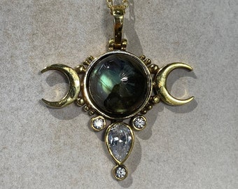 May include: Gold necklace with a triple moon pendant featuring a green labradorite gemstone and clear crystal accents.