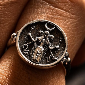 Op de afbeelding: Een zilveren ring met een gedetailleerd cirkelvormig ontwerp, met een centrale figuur en een halve maan. De ring heeft een getextureerde band en wordt om de vinger gedragen. Het ontwerp van de ring is ingewikkeld en gedetailleerd, met een vintage uitstraling.