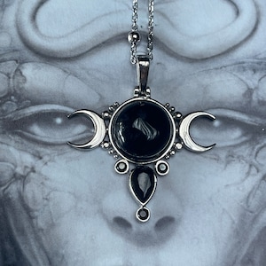 May include: Silver-toned pendant necklace featuring a central black stone surrounded by smaller black gems and crescent moon accents. The necklace has a delicate chain and a pendant with a gothic or celestial theme.