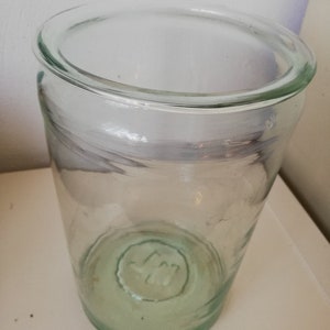 Könnte beinhalten: Ein klares Glasgefäß mit grünem Farbton und einer runden, geprägten Markierung auf dem Boden.