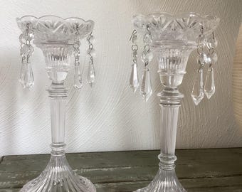 May include: Two clear glass candle holders with dangling crystal accents. The candle holders have a fluted base and a decorative rim. The crystals are teardrop-shaped and add a touch of elegance. These decorative candle holders are perfect for adding a touch of sparkle to any room.