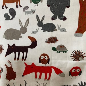May include: A white fabric with a repeating pattern of woodland animals, including foxes, owls, rabbits, deer, and a bear. The animals are illustrated in a cartoon style with bright colors.