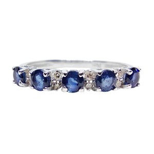May include: A silver ring with a row of oval, deep blue gemstones, alternating with smaller, clear stones. The ring is displayed on a white background, accentuating the gems' brilliance. A piece of jewellery.