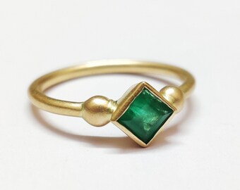 May include: A gold ring with a square emerald gemstone and two small gold balls on either side of the stone.