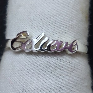 Puede incluir: Anillo de plata con la palabra "Believe" grabada en una fuente cursiva.