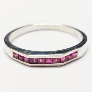 May include: A silver band ring with a row of small, square-shaped pink gemstones.
