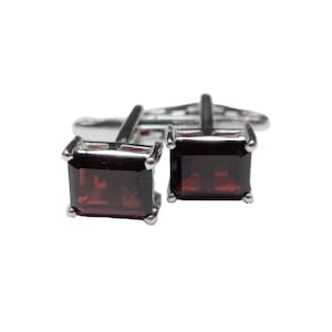 May include: A pair of silver cufflinks with square red gemstone accents.