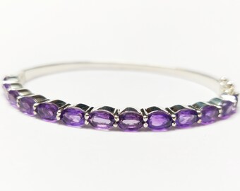 May include: A silver bangle bracelet with a row of oval-shaped amethyst gemstones.
