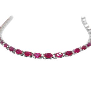 Op de afbeelding: Een delicate zilveren kettingarmband met ovale robijn edelstenen.