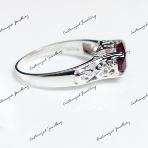 K&ouml;nnte beinhalten: Ein silberner Ring mit einem dunkelroten Edelstein, der in einem filigranen Design gefasst ist.