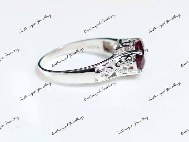 K&ouml;nnte beinhalten: Ein silberner Ring mit einem dunkelroten Edelstein, der in einem filigranen Design gefasst ist.