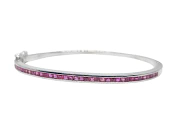 Puede incluir: Una pulsera de brazalete plateada con una fila de piedras preciosas rosas vibrantes, de corte cuadrado. La pulsera tiene un diseño simple y elegante con un pequeño cierre y una pequeña gema clara.