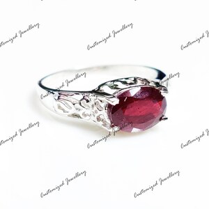 K&ouml;nnte beinhalten: Ein silberner Ring mit einem roten Edelstein, der in einem filigranen Design gefasst ist.