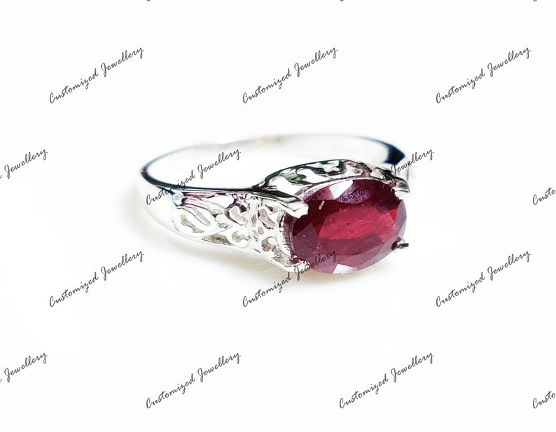 K&ouml;nnte beinhalten: Ein silberner Ring mit einem roten Edelstein, der in einem filigranen Design gefasst ist.