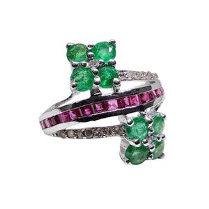 May include: A silver ring with a unique design, featuring clusters of green emeralds and a band of small, square-cut pink gemstones. The ring also has a band of small, clear gemstones.