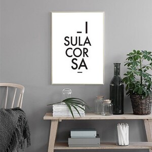 May include: A framed print with the text "- I SULA COR SA -" in black on a white background. The print is displayed on a wooden shelf with decorative items, including a green plant in a woven basket and glass jars.