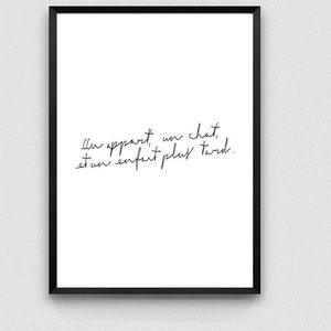 May include: A black framed print with a white background and a handwritten quote in French: "Il appartient un chat, et un enfant plus tard."