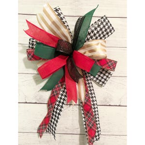 May include: A large, multi-colored bow made with red, green, black, white, and gold ribbon. The bow is tied with a knot in the center and has long tails.