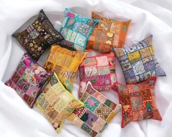 Puede incluir: Una colección de diez cojines de patchwork coloridos con varios patrones y bordados. Los cojines están hechos de una variedad de telas, incluyendo terciopelo, seda y algodón. Los cojines están dispuestos en un patrón aleatorio sobre una superficie blanca.