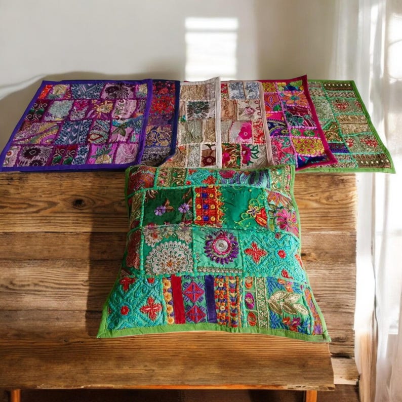May include: Four colorful patchwork throw pillows with embroidered details. The pillows are made of different fabrics and colors, including purple, green, pink, and white. The pillows are arranged on a wooden surface.