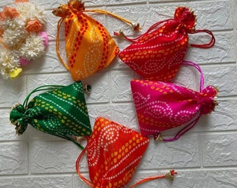 Può includere: Una collezione di cinque sacchetti con coulisse colorati, arancione, rosso, verde e rosa, ciascuno con un motivo a pois e un nappa dorata. I sacchetti sono disposti su uno sfondo di mattoni bianchi. Ideali per piccoli regali.