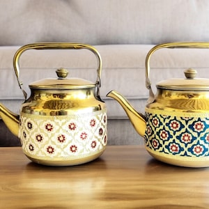 May include: Two gold tea kettles with ornate floral patterns. The kettle on the left has a white background with red and gold flowers. The kettle on the right has a blue background with gold and red flowers.