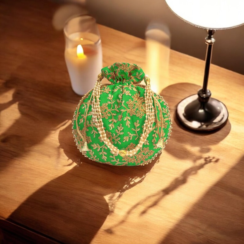 May include: A green drawstring bag with gold embroidery and pearl accents. The bag has a round shape and is decorated with floral patterns.