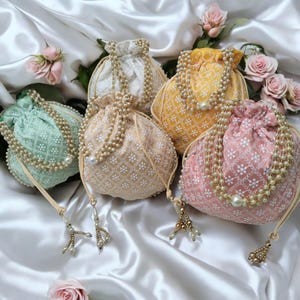 May include: Five drawstring bags with pearl embellishments. The bags are in various colors, including green, yellow, pink, and white. Each bag has a floral pattern and a pearl tassel.