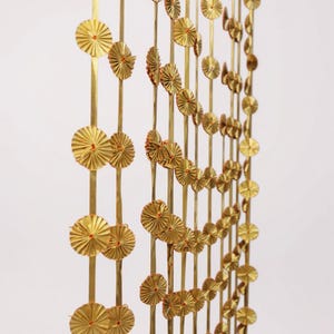May include: A decorative gold-colored curtain or room divider. The design features vertical strands adorned with small, circular, fan-like elements. The fan-like elements have a red center. The curtain is likely made of metal or a similar material.