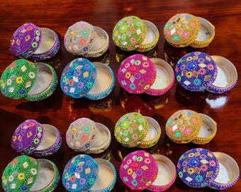 Può includere: Assortimento di 12 piccole scatole rotonde decorative con coperchi. Le scatole sono in metallo argentato e sono decorate con perline e paillettes colorate. I coperchi sono decorati con una varietà di motivi floreali in diversi colori, tra cui verde, blu, rosa, viola e oro.