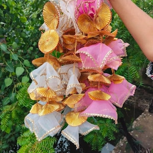 Może przedstawiać: Kolekcja dekoracyjnych wiszących ozdób z białej i różowej przezroczystiej tkaniny, zaakcentowanych złotymi, wachlarzowatymi zdobieniami. Ozdoby są obszyte złotymi obwódkami i zawieszone z centralnego punktu.