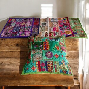 May include: Four colorful patchwork throw pillows with embroidered details. The pillows are made of different fabrics and colors, including purple, green, pink, and white. The pillows are arranged on a wooden surface.