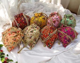 May include: A set of eight colorful drawstring bags with floral patterns and pearl embellishments. The bags are made of fabric and have a round shape. They are arranged in a circle on a white surface.