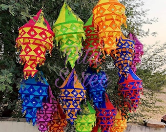 May include: A collection of colorful, multi-layered fabric lanterns with intricate geometric patterns and mirror accents. The lanterns are hanging from a tree branch and are perfect for adding a festive touch to any occasion.