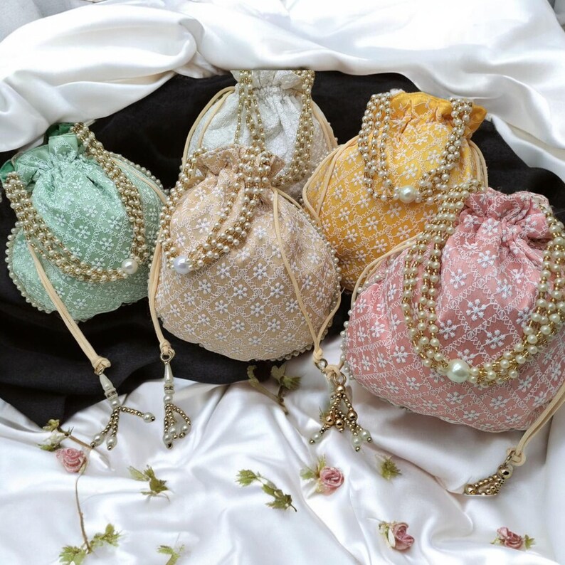 May include: Five drawstring bags with pearl embellishments. The bags are in various colors, including green, beige, yellow, and pink. Each bag has a floral pattern.