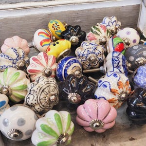 May include: A collection of colorful ceramic drawer knobs with various patterns and designs. The knobs are in a variety of shapes, including round, square, and oval. Some of the knobs have floral patterns, while others have geometric patterns.