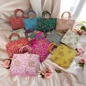 Könnte beinhalten: Eine Sammlung von 10 bunten bestickten Handtaschen mit goldenen Details. Die Handtaschen haben Holzgriffe und sind auf einer hellrosa Stoffoberfläche angeordnet.
