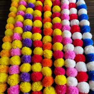 K&ouml;nnte beinhalten: Eine Girlande aus bunten Pompons in Gelb, Orange, Rot, Rosa, Lila, Wei&szlig; und Blau. Die Pompons sind zu einer festlichen Dekoration zusammengef&uuml;gt.