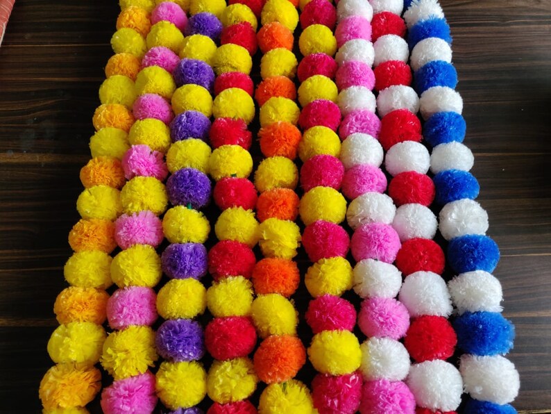 K&ouml;nnte beinhalten: Eine Girlande aus bunten Pompons in Gelb, Orange, Rot, Rosa, Lila, Wei&szlig; und Blau. Die Pompons sind zu einer festlichen Dekoration zusammengef&uuml;gt.