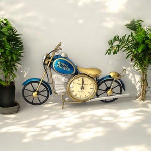 Könnte beinhalten: Eine blaue und silberne Motorrad-Uhr aus Metall mit goldenem Zifferblatt und schwarzen Zeigern. Das Motorrad trägt den Schriftzug "Royal Enfield" an der Seite.